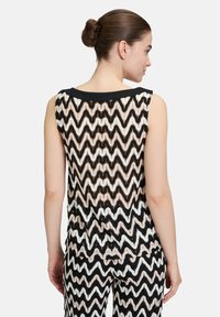 Schwarzes und beiges ärmelloses Top mit Zickzackmuster, das einen schwarzen Ausschnitt und durchscheinendes Material aufweist, von hinten gezeigt.