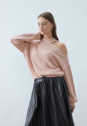 Light pink knitted sweater with an off-shoulder design and high collar, paired with a pleated black faux leather skirt.