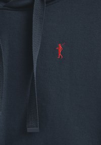 Marinblå hoodie med en röd broderad logotyp av en golfare. Texturerat tyg med en känguruficka och dragsko-huvud.