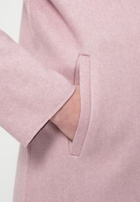 Ροζ ανοιχτό παλτό από μαλλί με απαλή υφή, διαθέτει κρυφό τσέπη στο πλάι και μανίκι με ίσια κοπή. Μινιμαλιστικός σχεδιασμός.