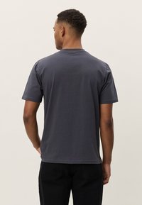 Pelēka kokvilnas T-krekls ar īsām piedurknēm, apaļu kakla izgriezumu un brīvu piegriezumu, skatīts no aizmugures ar gludu tekstūru un vienkāršu dizainu.