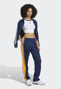 Navy tracksuit with orange stripes, cropped white top, and elastic waistband. Includes three white stripes on sleeves and pants. Lightweight fabric.