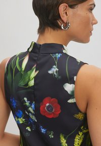Floral-gedrukt jurk in donkere stof met felrode, blauwe en groene bloemen. Heeft een hoge kraag en ritssluiting aan de achterkant.