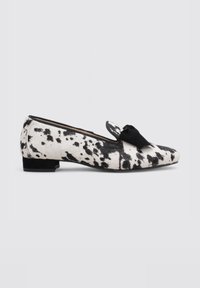Mocasines con estampado de vaca en blanco y negro, con parte superior de tela, un pequeño lazo negro como acento en el empeine y un tacón bajo y cuadrado.