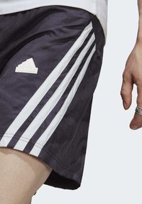 Pantaloni sportivi navy con tre righe bianche e logo Adidas. Realizzati in materiale leggero, presentano una finitura testurizzata e una vestibilità comoda.