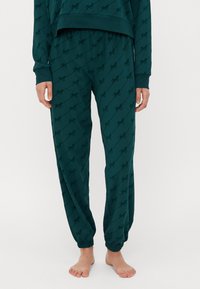 Teelee pyjama-asu, jossa on joustava vyötärö ja kapenevat hihansuut, ja joka sisältää toistuvan logo-kuvion koko ajan. Pehmeä, sileä kangas.
