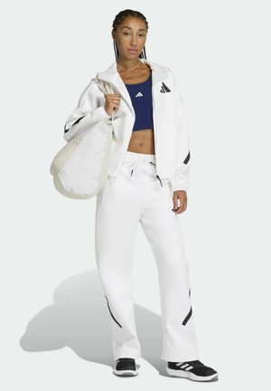 White athletic jacket with black accents, navy crop top, white pants, and black sneakers. Holding a cream shoulder bag.