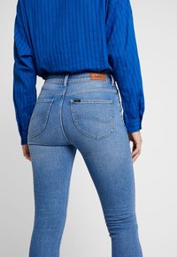 Vaqueros de mezclilla azul con corte slim, que cuentan con un parche de cuero en la cinturilla y costuras contrastantes en los bolsillos traseros.