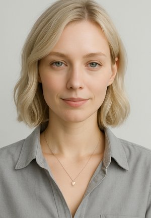 Smal silverkedja med ett litet hjärtanhänge. Modellen bär en grå skjorta med knappar mot en neutral bakgrund.