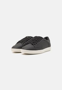 Schwarze Sneaker mit strukturiertem Obermaterial, Schnürverschluss und kontrastierender weißer Gummisohle. Minimalistisches Design mit Seitenakzenten.