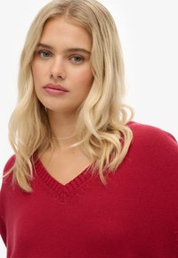 Maglione rosso a maglia con scollo a V, caratterizzato da un motivo testurizzato e bordino a costine intorno all'collo. Tessuto morbido e vestibilità comoda.