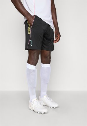Sorte sports shorts med gule og teal accenter, hvide knælange sokker og hvide fodboldstøvler. Har et logo på shortsene.