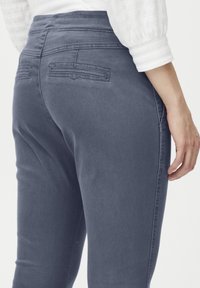 Jeans de mezclilla gris con una textura suave, cintura alta y bolsillos traseros. La vista lateral muestra un diseño ajustado y detalles de costura limpios.