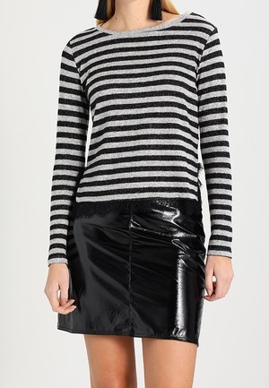 Kobieta ubrana w czarno-szarą, paskowaną bluzkę z długim rękawem i koronkowym wykończeniem, w połączeniu z błyszczącą czarną mini spódnicą z winylu.