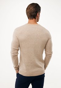 Maglione lavorato a maglia beige con maniche lunghe, scollatura rotonda e polsini a coste. Tessuto morbido, vestibilità casual e design semplice.