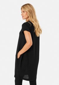 Robe noire à manches courtes avec une silhouette décontractée, dotée de poches latérales et d'un ourlet hi-low subtil, confectionnée dans un tissu doux et léger.
