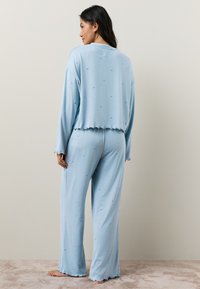 Lyseblåt pyjamasæt lavet af blødt stof, inkluderer en kort top med bølgede kanter og løstsiddende bukser, begge med små stjernemønstre.