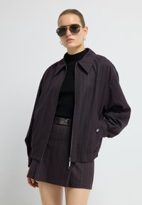 Oversized, donkerpaarse bomberjack met streepdessin en een frontale rits, gecombineerd met een aansluitend zwart geribd topje en een bijpassende rok.