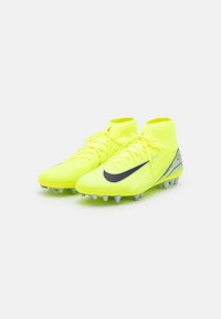 Des crampons de football jaune vif avec un design mi-haut, une tige texturée, un accent de swoosh noir et des détails gris sur les semelles et les côtés.
