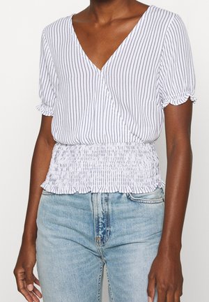 White top with vertical navy stripes, V-neck, short gathered sleeves, and a smocked waist. Paired with light blue jeans.