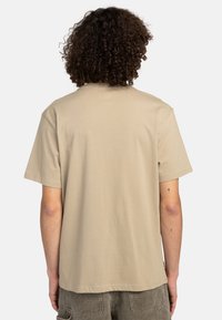 Camiseta de algodón beige con un ajuste relajado, mangas cortas y cuello redondo. Textura suave sin patrones ni acentos visibles.