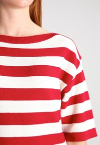 Gestreiftes Strickoberteil in Rot und Weiß mit weitem Rundhalsausschnitt und kurzen Ärmeln, das ein strukturiertes Stoffmuster und einen gerippten Saum aufweist.