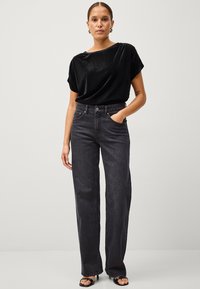 Sort velour kortærmet top parret med højhalset, vide ben mørkegrå jeans. Modellen bærer sorte hæle sandaler.