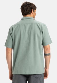 Short-sleeve, light green shirt with a textured fabric, a classic collar, and a straight hem. Back view shows a smooth, even fit.
