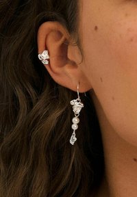 Silver earrings featuring a textured design with a floral motif, adorned with two white pearls and a delicate charm hanging below.