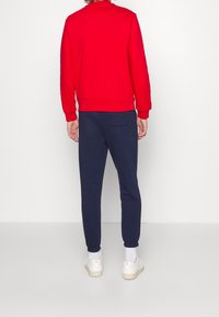 Punainen collegepaita ja tummansiniset collegehousut, molemmat pehmeästä kankaasta. Collegepaidassa on pyöreä pääntie ja resorireunat hihansuissa, housuissa on takatasku.