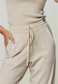Beige gestrickte Jogginghosen mit einem Kordelzugbund und seitlichen Taschen. Weicher Stoff, lockere Passform und sichtbare Nähedetails.
