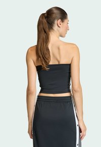 Čierny top bez ramienok s hladkou textúrou, spárovaný s čiernou sukňou s vysokým pásom, ktorá má biele postranné gombíky a kontrastné pruhy.