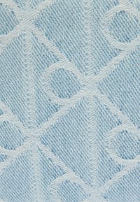 Υφασμα από ανοιχτό μπλε τζιν με υφή που περιλαμβάνει διαγωνίες γραμμές και κυκλικές λεπτομέρειες, δημιουργώντας βάθος και οπτικό ενδιαφέρον.