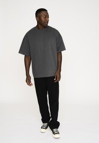 Kortærmet crew neck t-shirt i grå, parret med sorte vide bukser og sorte sneakers med hvide såler, mod en neutral baggrund.