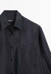 Chemise noire à finition satinée avec boutons, col pointu, poche poitrine et étiquette de marque Massimo Dutti visible à l'intérieur du col.