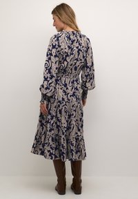 Mornarsko modra obleka z belim paisley vzorcem, elastičen pas, dolgi rokavi, nabrani rob in v kombinaciji s smešnimi rjavimi škornji do kolen.