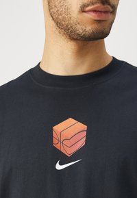 Camiseta de algodón azul marino con un gráfico de un cubo naranja con forma de corazón y el logotipo de Nike en blanco debajo.