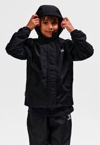 Czarna wodoodporna kurtka z kapturem, wyposażona w elastyczne mankiety i pełny zamek błyskawiczny. Na piersi znajduje się logo, a do kompletu dołączone są czarne spodnie.