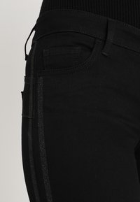 Svarta denimbyxor med slim fit, utrustade med en glänsande svart rand längs sidan och standardfickor bak.