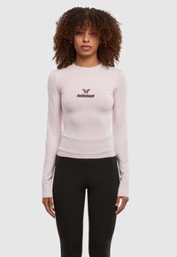 Langermet, lys rosa tettsittende topp med rund hals og maroon "felicious" logo i midten, kombinert med svarte leggings.