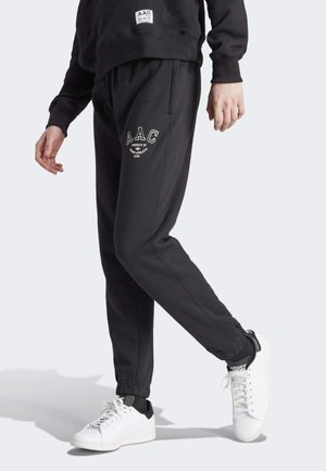 Zwarte sweatpants met elastische boorden, met een wit logo op de dij, gecombineerd met witte sneakers met zwarte accenten.