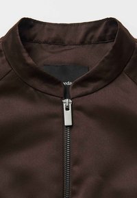 Bruine bomberjackkraag met een gladde satijnen afwerking, voorzien van een rits aan de voorkant en een zwart stoffen label onder de kraag.