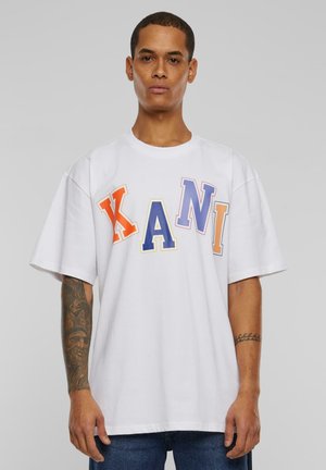 Vit bomulls t-shirt med djärva flerfärgade bokstäver "KANI" i orange, gult, blått och lila. Avslappnad passform med korta ärmar.