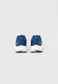 Μπλε αθλητικά παπούτσια με επάνω μέρος από δίχτυ, λευκή μεσαία σόλα και μπλε εξωτερική σόλα. Διαθέτουν πράσινες λεπτομέρειες και λογότυπο κοντά στη φτέρνα.