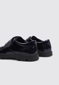 Chaussures en cuir verni marine avec une finition lisse, bout rond et semelle en caoutchouc noire. Dotées d'une sangle velcro sur le côté pour un maintien sécurisé.