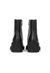 Bottines en cuir noir avec un bout carré, des zips sur les côtés et une semelle épaisse. Texture lisse et détails de design minimalistes.
