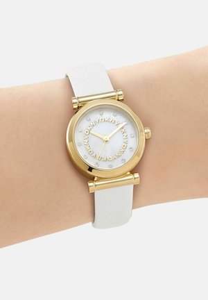 Goldene runde Uhr mit weißem Lederarmband am Handgelenk, mit DKNY-Logo-Kreis und Kristall-Stundenmarkierungen auf weißem Zifferblatt.