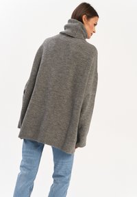 Szary, prą�żkowany sweter typu golf z luźnym krojem i długimi rękawami, pokazany z tyłu. W połączeniu z jasnoniebieskimi dżinsami. Prosty design.