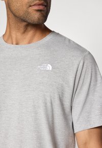 Ανοιχτό γκρι βαμβακερό μπλουζάκι με στρογγυλή λαιμόκοψη. Διαθέτει λευκό κεντημένο λογότυπο στο πάνω αριστερό μέρος του στήθους. Μαλακή υφή, κοντά μανίκια.