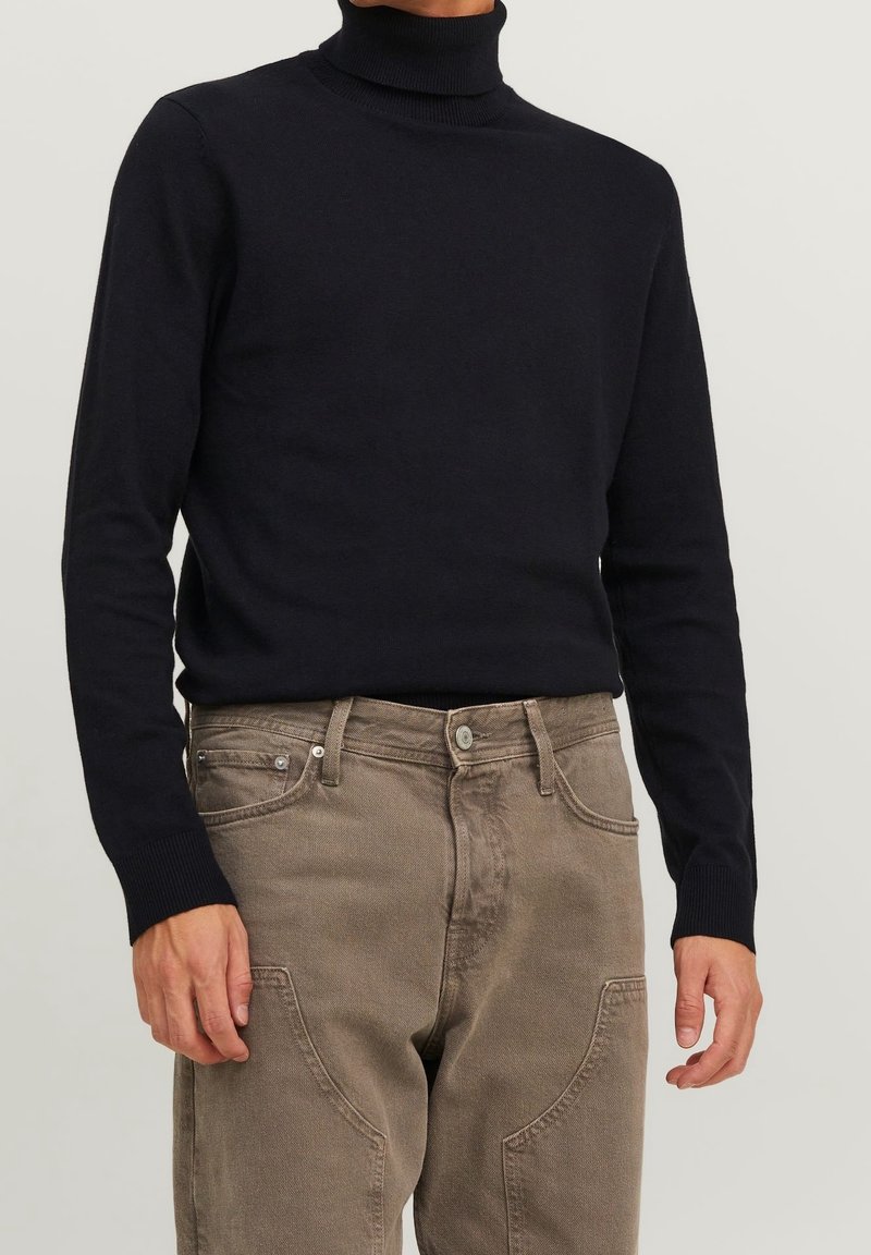 Pull à col roulé bleu marine en tricot doux, avec des manches longues et des poignets côtelés, associé à un pantalon en denim beige avec des poches avant.